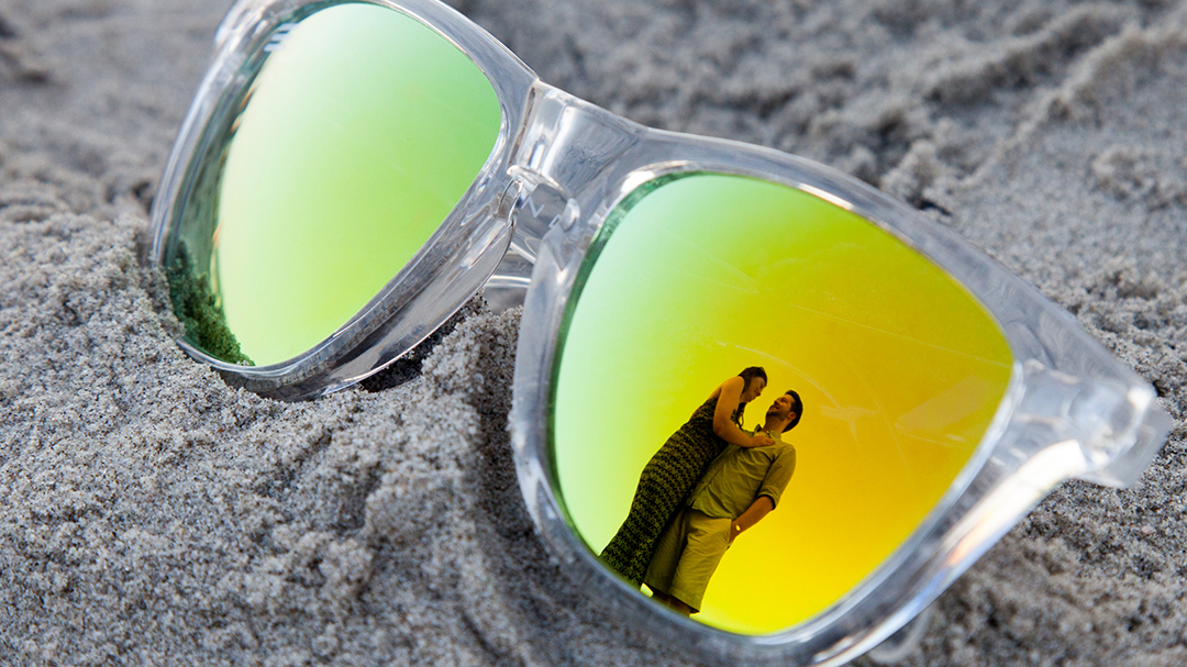 Sunglasses on the beach with the reflection of an engaged couple in them. 